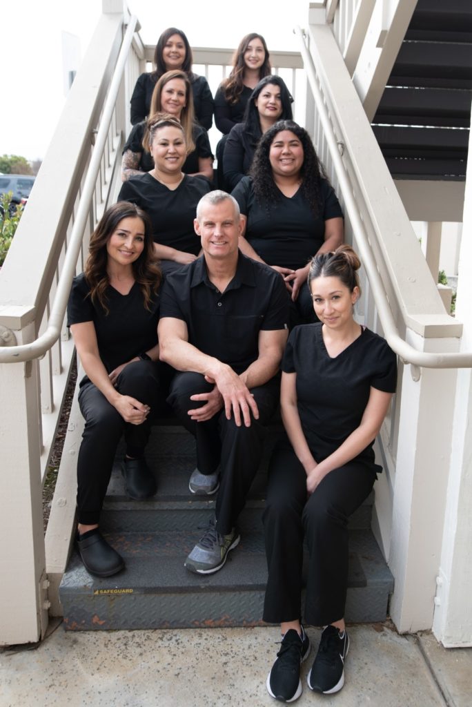 Photo of Dr. Darnell dental team sitting together on stairs at dentist office in Hollister, CA